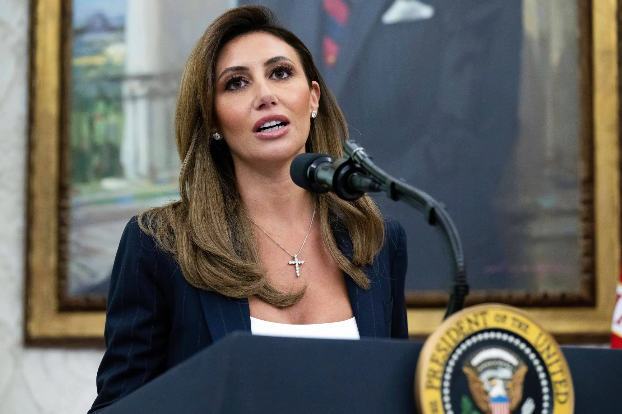 Alina Habba speaking at a podium bearing the presidential seal
